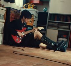 a young man sitting on the floor playing an electric guitar with his legs spread out