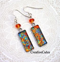 Bright orange faceted crystal beads sit atop colorful mandala art images beneath smooth glass cabochons in shiny stainless steel pendant trays...Boho Beauties! Uniquely hand crafted with these quality materials: ~ Stainless steel pendant trays with sealed images & glass cabochons ~ Silver plated lead & nickel-free French style ear wires ~ Silicone earring backs to keep earrings securely in ears Measuring 2 inches from the tops of the ear wires to the bottom of the charms, these earrings are ligh Colorful Bohemian Glass Jewelry, Artistic Orange Dangle Jewelry, Artistic Orange Nickel-free Earrings, Orange Jewelry Gift, Orange Fusion Jewelry Gift, Vibrant Orange Jewelry For Festival, Vibrant Orange Festival Jewelry, Artistic Multicolor Nickel-free Jewelry, Vibrant Orange Dangle Jewelry