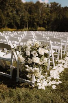 white chairs are lined up in the grass for an outdoor ceremony with flowers on them