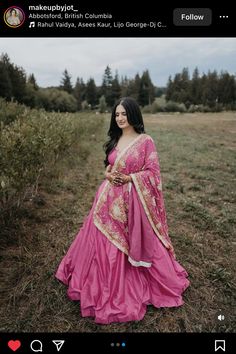 a woman in a pink dress is standing in the middle of a field with trees