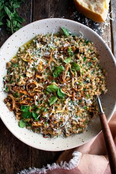 a white bowl filled with food on top of a wooden table next to some bread