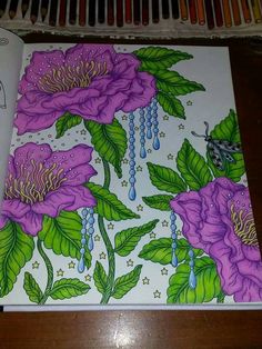 a drawing book with purple flowers and green leaves on the cover, next to colored pencils