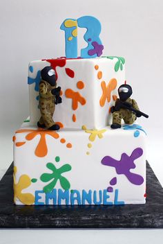 a multi - tiered birthday cake decorated with fondant paint splatters and two figurines