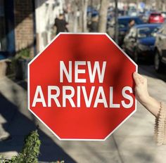 a person holding up a red stop sign that says new arrivals on the side of a street