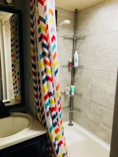 a bathroom with a shower curtain, sink and bathtub in the foreground is a tiled wall