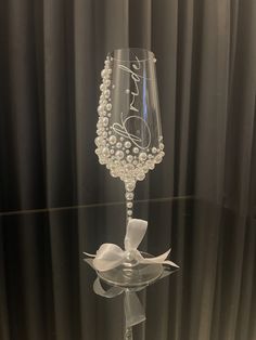 a wine glass that has been decorated with pearls and a bow on the side, sitting on a table