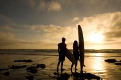 two people standing on the beach holding surfboards