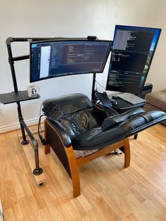 two computer monitors sitting on top of a black chair in front of a wooden floor