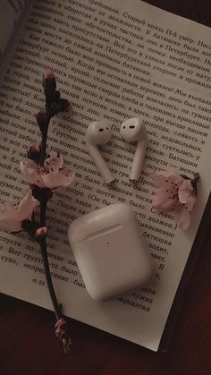 an apple airpods sitting on top of a book next to some pink flower buds