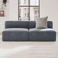 a gray couch sitting in front of a window next to a white rug on top of a hard wood floor