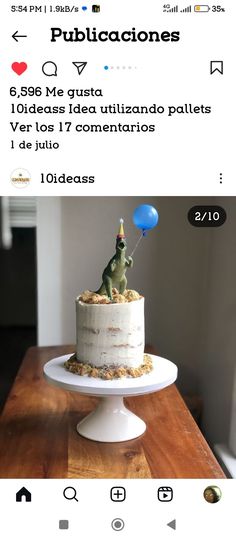 a white cake with a dinosaur on top sitting on a table next to a blue balloon