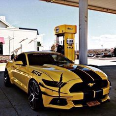 a yellow mustang parked in front of a gas station with black and white stripes on it