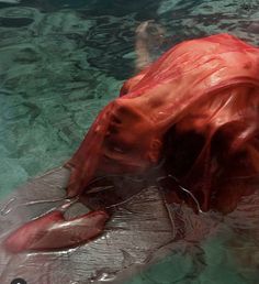 a woman floating in the water wearing a red dress