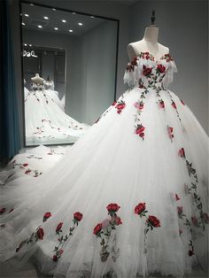 a white dress with red roses on the skirt is displayed in front of a mirror