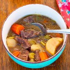 a bowl of beef and vegetable soup with a spoon in it on a wooden table