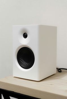 a white square speaker sitting on top of a wooden table next to a black cord