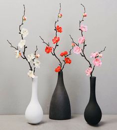 three vases with flowers in them sitting on a table next to each other,