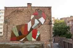 a large painting on the side of a brick building in an urban area with buildings around it