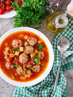 a bowl of soup with meatballs, tomatoes and parsley next to it on a table