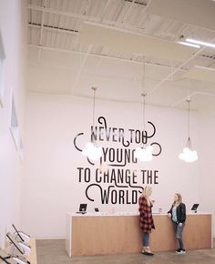 two women standing in front of a counter with the words never top young to change the world on it