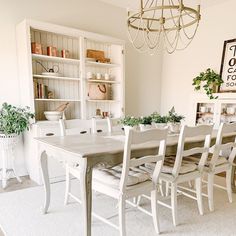 a dining room table with white chairs in front of it and bookshelves behind it