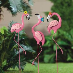 three pink flamingos are standing in the grass with flowers on their heads and legs