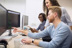 three people sitting at a desk working on computers and looking at each other's screens