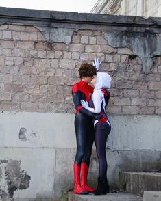 two people dressed as spider - man and catwoman hugging each other on some steps