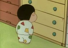 a little boy standing in front of a dresser with drawers on it's sides