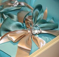 two blue and gold gift boxes with bows on them, one has a diamond brooch