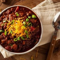 a white bowl filled with chili and cheese on top of a wooden table next to a napkin