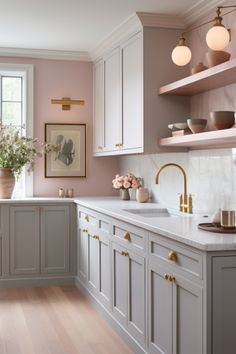 a kitchen with pink walls and white cabinets, gold pulls on the cupboards in front of the sink