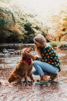 a woman kneeling down next to a brown dog on top of a muddy river bank