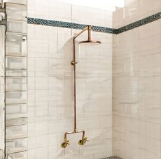 a bathroom with white tile and gold faucet shower head, toilet seat and hand rail