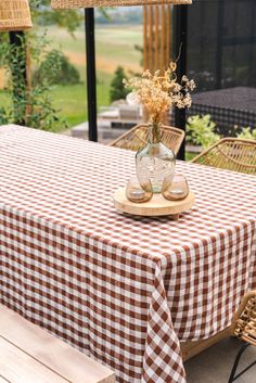 a checkered table cloth with flowers in a glass vase on it and two wicker chairs