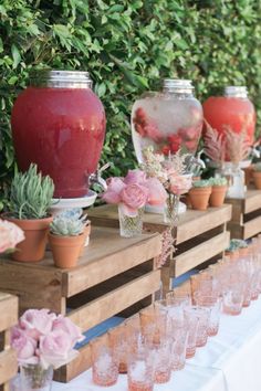 a table topped with lots of vases filled with flowers next to plants and wine glasses