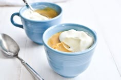 two blue mugs filled with ice cream and caramel sauce on a white table