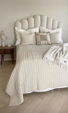 a white bed with pillows and blankets on it in a room that has wood floors