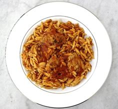 a white plate topped with pasta covered in meat and sauce on top of a marble table