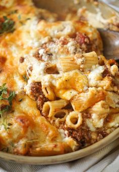 a close up of a plate of pasta with meat and cheese on it, next to a spoon