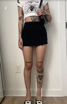 a woman with tattoos is standing in front of a wall and holding a cell phone