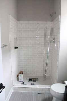 a white tiled bathroom with a toilet and shower