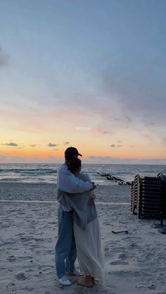 a man and woman hug on the beach at sunset with an ocean in the background