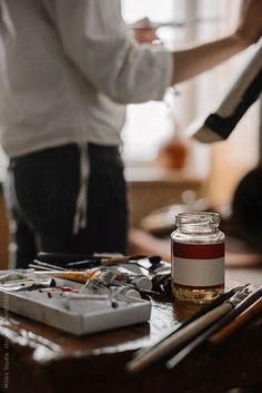 a person standing in front of a table with art supplies and paintbrushes on it