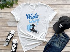 This Wake Surf t-shirt is the perfect addition to any surfer's wardrobe!  Featuring a stylish graphic design of a wake surfer catching a wave, this shirt is perfect for anyone who loves to surf and wants to show off their passion for the sport.  Not only is this t-shirt comfortable and stylish, but it is also durable and made to last. Whether you're hitting the beach or just running errands around town, this t-shirt is the perfect choice for any casual occasion. So why wait? Add this Wake Surf t-shirt to your collection today and start showing off your love for surfing in style! * 100% combed and ring-spun cotton (Heather colors contain polyester) * Fabric weight: 4.2 oz/yd² (142 g/m²) * Pre-shrunk fabric * Side-seamed construction * Shoulder-to-shoulder taping This product is made especia Casual Crew Neck T-shirt For Water Sports, Casual Graphic Print T-shirt For Water Sports, Wake Surfing, Surf T Shirts, Surf Tshirt, Design Graphique, Running Errands, Surfing, Bathing Beauties