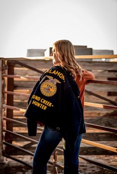 a woman standing in front of a fence wearing a jacket that says canyon creek hunter