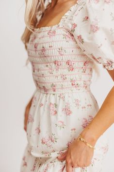 If you're looking ahead to blooming flowers and sunshine, you need this beautiful dress to help herald in springtime! This gem is crafted from a charming, 100% cotton floral print, and features a smocked bodice with sleeves that can be worn on or off the shoulders. It's a must-have for baby showers, gender reveals, or christenings! The Harper is sure to sell out, so don't wait to snag yours! FIT: Runs true to size. The bodice is stretchy and smocked, but the rest of the dress does not have stret Cottagecore Floral Print Flowy Dress, Flowy Floral Print Cottagecore Dress, Pink Floral Dress With Smocked Back For Spring, Spring Floral Dress With Smocked Bodice For Garden Party, Floral Dress With Smocked Bodice For Spring Garden Party, Floral Dress For Spring Garden Party, Flower-shaped Dresses For Spring Garden Party, Cottagecore White Midi Dress With Floral Print, Feminine Rose Print Dress