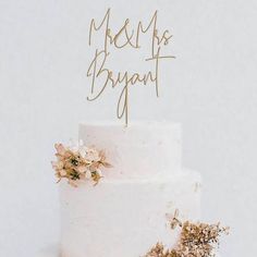 a white wedding cake with gold lettering and flowers