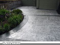 a concrete patio with plants and flowers in the corner, next to a garage door