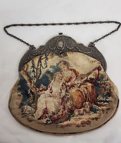 "This is a very elegant circa 1800's Victorian purse or tapestry bag.  Featuring needlework of two ladies or possibly a mother and daughter, sitting outdoors with their puppy while playing music and reading. There is a basket full of picked flowers and what looks to be a water jug with ladle.  On the back it has possibly the mother dog sitting alongside pink roses, a shepherdess's hook and a hat.     The top of this purse is framed with a very detailed embossed silver frame which features flowin Victorian Purses, Picked Flowers, Embellished Purses, Victorian Photos, Two Ladies, Tapestry Bag, Metal Leaves, Water Jug, Beaded Purses